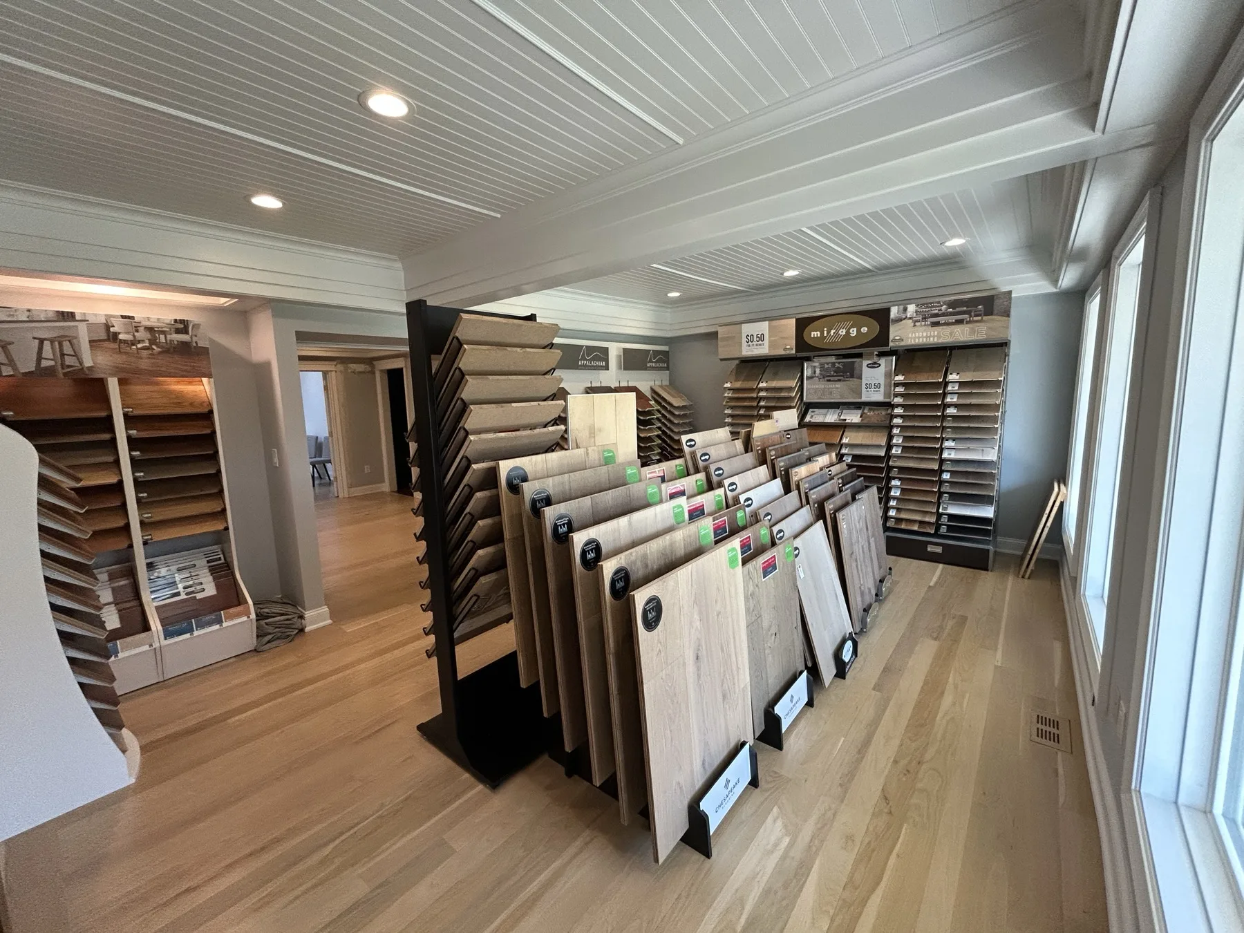 Racks of full-size hardwood boards on a laid oak floor in the Gorsegner Brothers showroom, with Appalachian, Mirage and Chesapeake displays along the wall