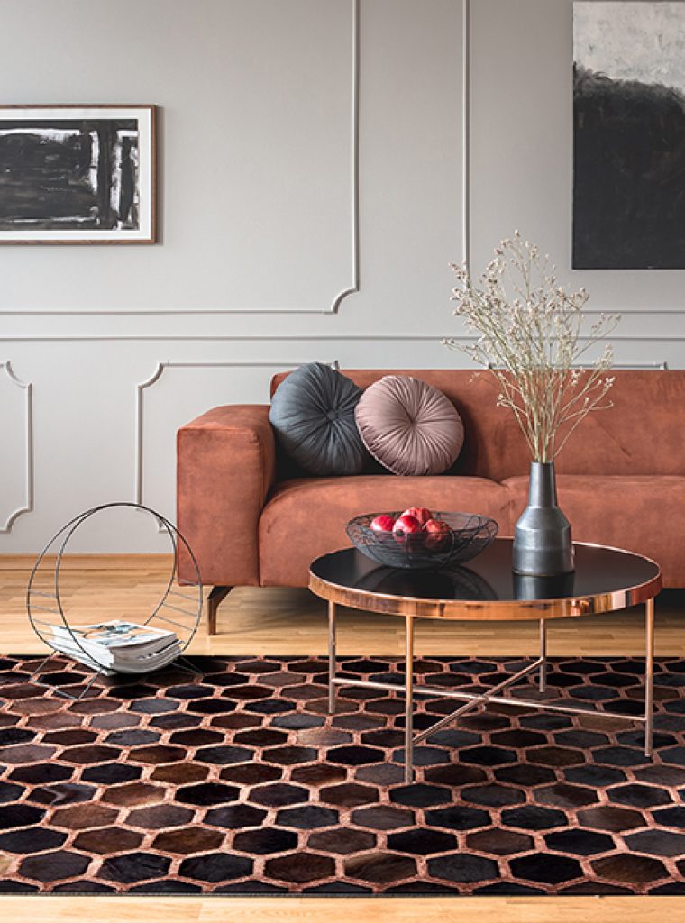 Flowers in vase and red fruits in bowl on wooden coffee table in elegant living room interior with ginger sofa